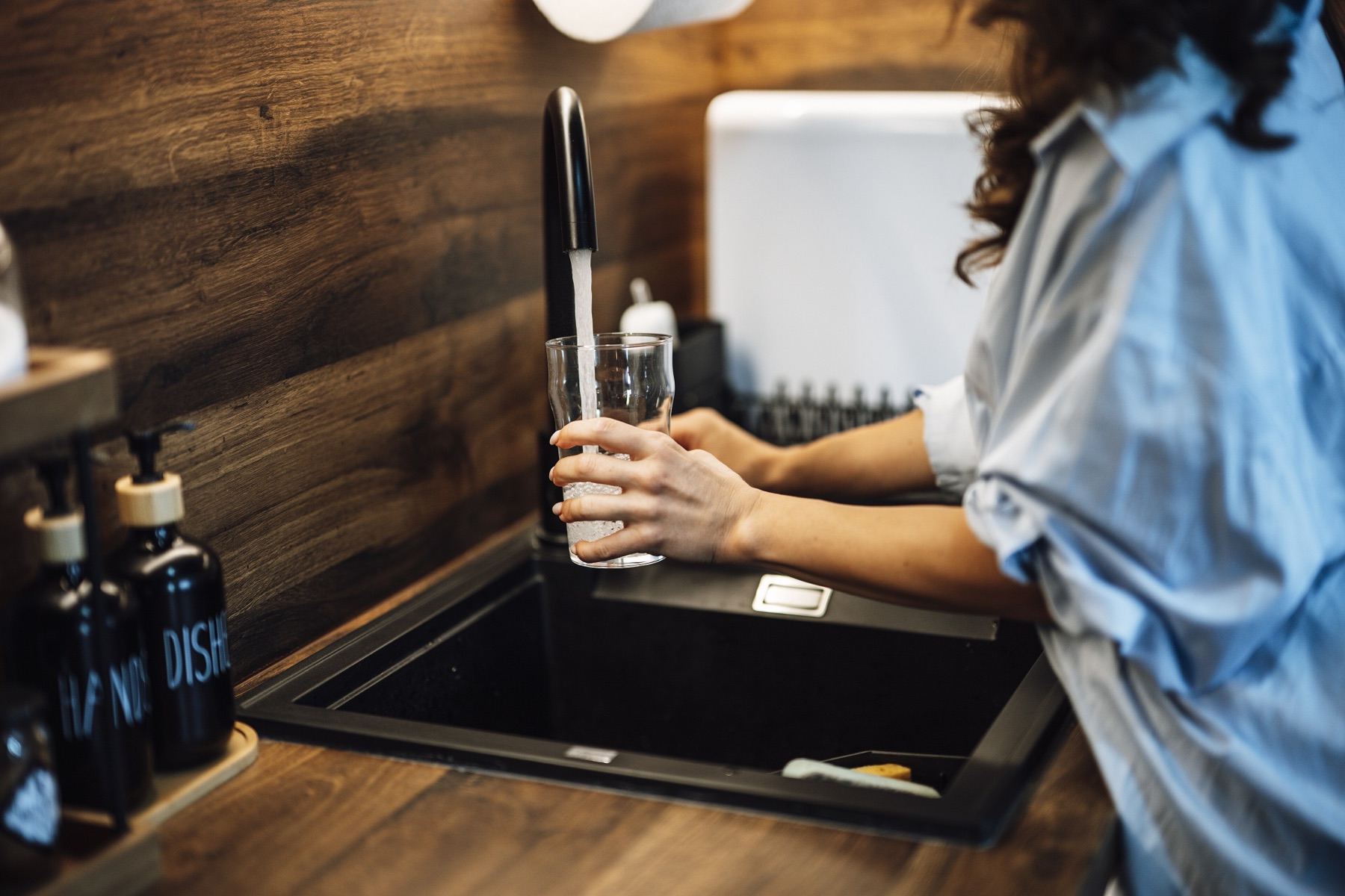 A person filling a glass of water at a kitchen tap